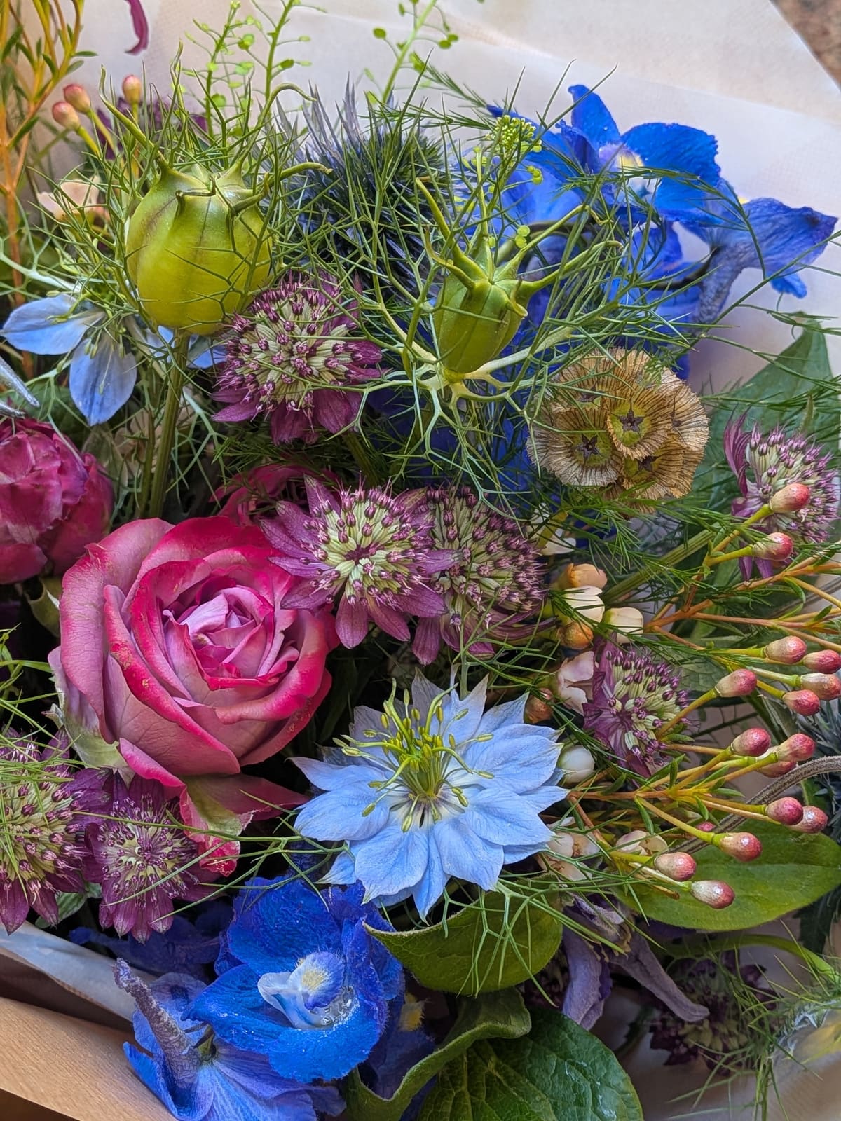 A close-up of blue delphinium, nigella, astrantia and a deep pink rose in a wild hand-tied bouquet